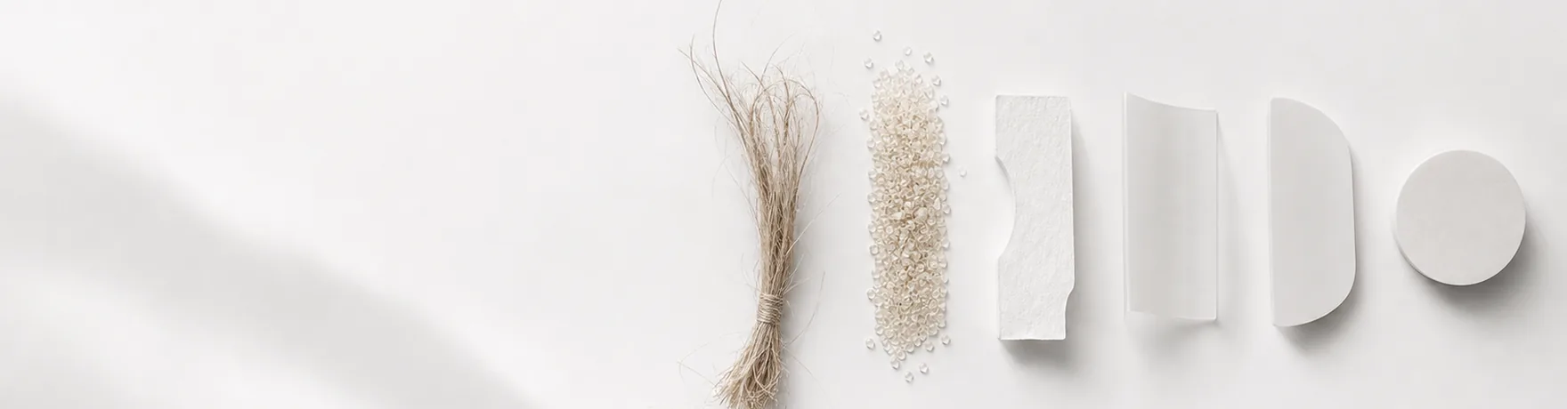 バイオプラスチックを表すイメージ。白い台に植物繊維の束、淡い色の樹脂ペレット、厚手の白いシート、透明フィルム、半円板、丸い円盤が横一列に並んでいる